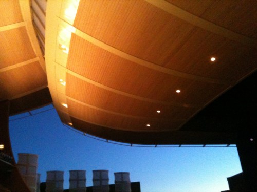 A modern architectural structure with a curved wooden ceiling and soft lighting against a twilight sky.