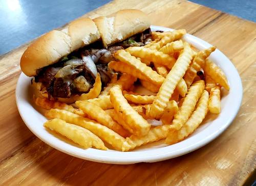 A plate with a sandwich filled with meat and vegetables, accompanied by a side of crinkle-cut fries.