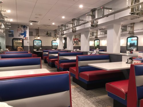 Interior of a retro diner featuring red and blue booths, bright lighting, and a clean, modern design.