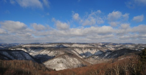 A panoramic view of snow-covered mountains under a blue sky with fluffy clouds.