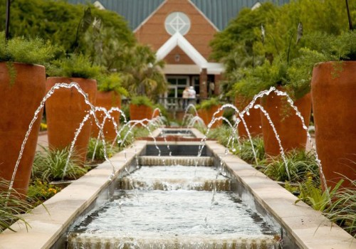 A serene garden scene featuring a water fountain with flowing water, surrounded by lush greenery and decorative pots.