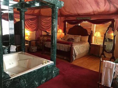 Luxurious hotel room featuring a marble bathtub, elegant bed, and rich red decor with soft lighting.