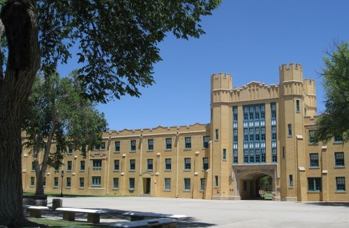 Historic building with castle-like towers, surrounded by trees and a clear blue sky.