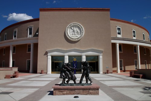 Exterior view of a round building with a seal, featuring a bronze statue of three figures in front.