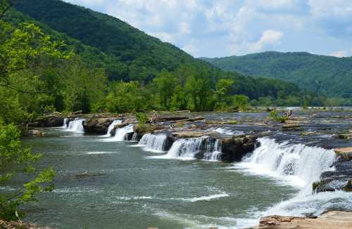 A serene landscape featuring cascading waterfalls surrounded by lush green hills under a blue sky.