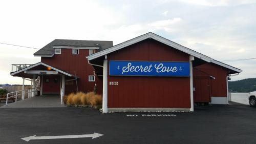 Red building with a blue sign reading "Secret Cove," surrounded by a parking area and grass.