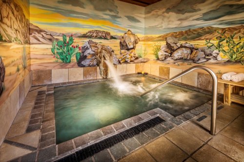 A serene spa room with a hot tub, surrounded by desert-themed murals and natural stone accents.