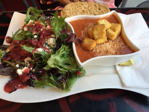A bowl of tomato soup with croutons, served alongside a fresh salad with mixed greens and a slice of bread.