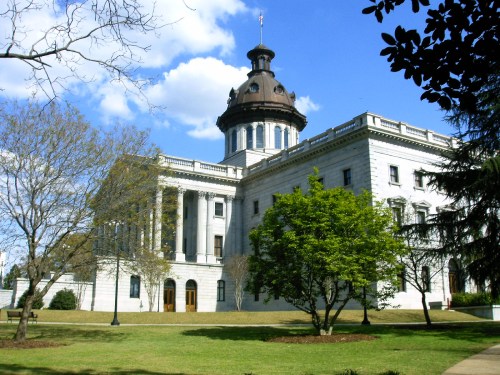 Historic building with a dome, surrounded by trees and blue sky, showcasing classic architectural features.