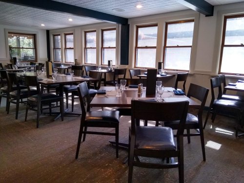 A spacious restaurant interior with empty tables, chairs, and large windows letting in natural light.