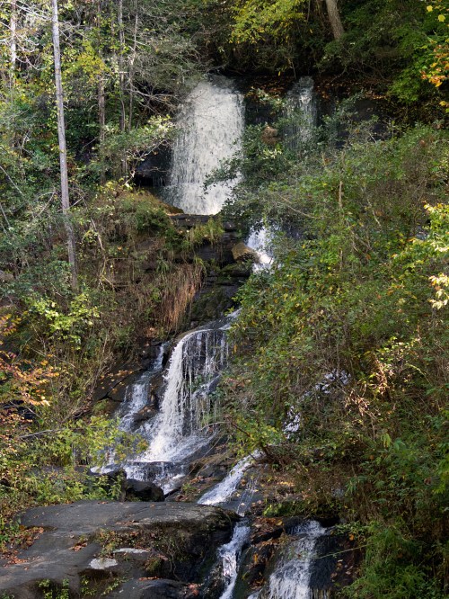 A serene waterfall cascading down rocky terrain, surrounded by lush green foliage and trees.