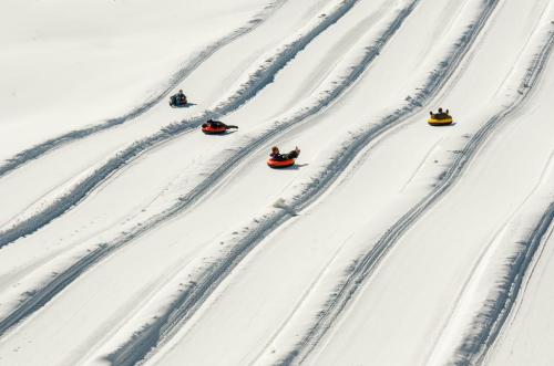 People tubing down snowy slopes, leaving tracks in the fresh snow, with colorful tubes in red, yellow, and blue.