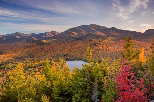 A vibrant autumn landscape featuring mountains, colorful foliage, and a serene lake under a clear blue sky.