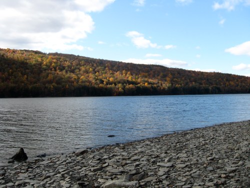 A serene lake surrounded by a forest of colorful autumn foliage under a partly cloudy sky.