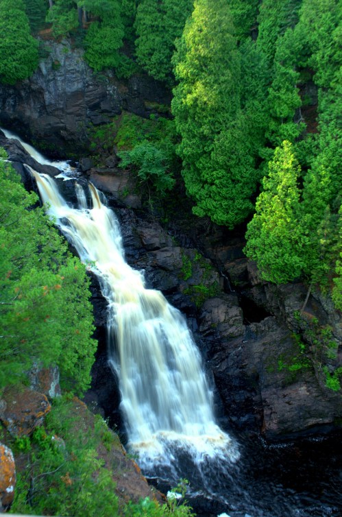 A cascading waterfall flows through a rocky gorge, surrounded by lush green trees.