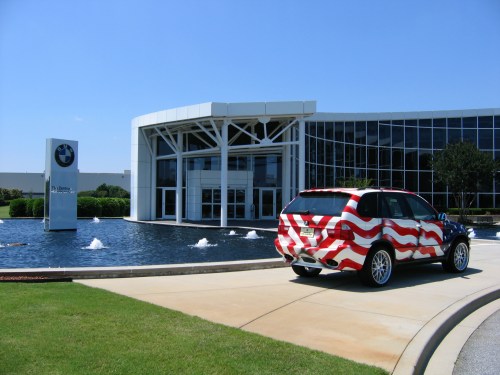 A BMW dealership with a fountain and a car wrapped in red and white stripes parked in front.