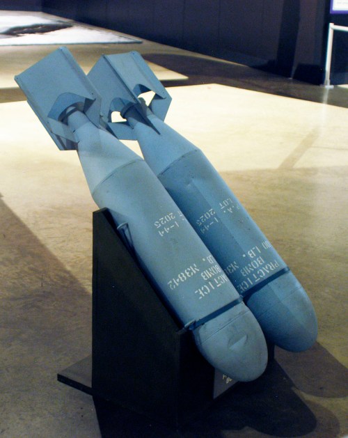 Two large, gray bombs displayed on a stand in a museum setting, with visible markings and labels.