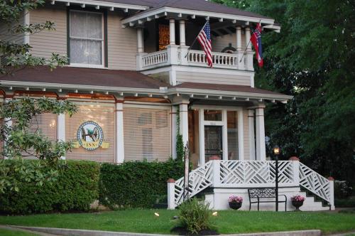 A charming inn with American and Mississippi flags, surrounded by greenery and flowers, featuring a welcoming porch.