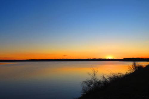 A serene sunset over a calm lake, with vibrant orange and blue hues reflecting on the water's surface.