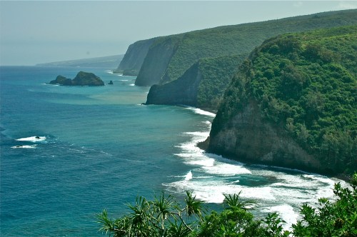 A scenic coastal view featuring lush green cliffs, rocky outcrops, and gentle waves lapping at the shore.