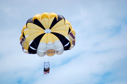 A colorful parasail with two people soaring high in the sky against a backdrop of clouds.