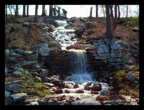 A serene waterfall cascading over rocks, surrounded by trees and natural foliage in a peaceful outdoor setting.