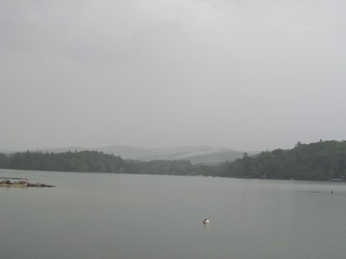 A calm lake surrounded by misty mountains under a gray, overcast sky.