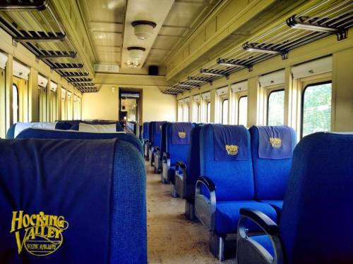 Interior of a vintage train car with blue upholstered seats and large windows, featuring a clean, spacious aisle.