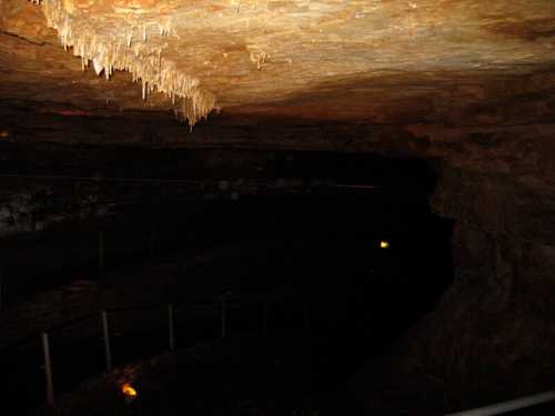 A dimly lit cave interior with stalactites hanging from the ceiling and a winding path leading into darkness.