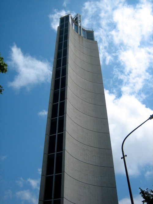 A tall, modern building with a curved facade against a blue sky with clouds.