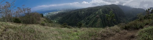 Panoramic view of lush green mountains and coastline under a partly cloudy sky.
