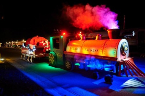 A colorful train decorated with lights, resembling the Polar Express, emits smoke in a nighttime setting.