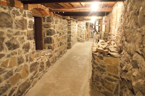 A dimly lit stone corridor with rough walls and a concrete floor, featuring piles of stones along the sides.