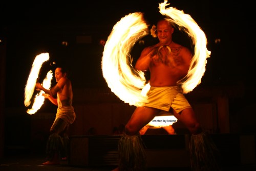 Two performers dance with flaming poi, creating bright circles of fire against a dark background.
