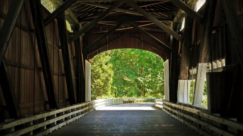 View from inside a covered bridge, showcasing wooden beams and a glimpse of greenery outside.