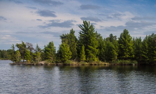A serene lake scene featuring an island with lush green trees under a partly cloudy sky.