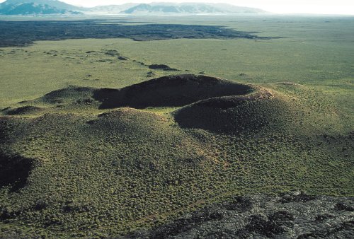 Aerial view of green volcanic hills surrounded by a vast, flat landscape under a clear sky.