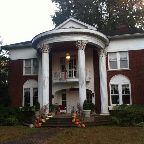 A large brick house with white columns, pumpkins on the steps, and a flag hanging from the porch.