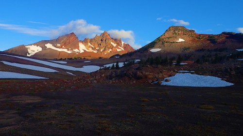 Scenic mountain landscape with rocky peaks, patches of snow, and a clear blue sky.