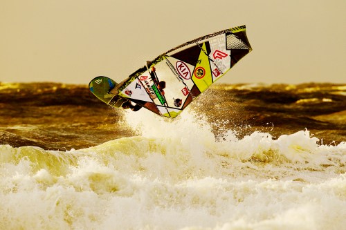 A surfer performs a jump over a wave, showcasing skill and excitement against a golden sky.