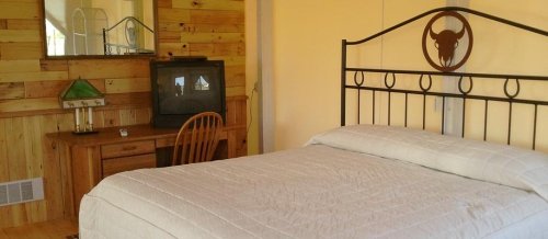 A cozy bedroom with a wooden wall, a bed, a desk, a chair, and a TV in the corner.