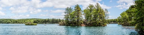 A serene lake surrounded by lush green trees under a partly cloudy sky.