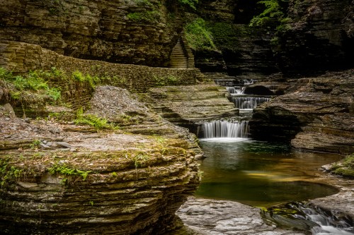 A serene landscape featuring cascading waterfalls and smooth stone formations surrounded by lush greenery.