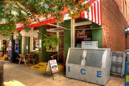 A vintage storefront with a red and white awning, featuring a sign for ice cream and a vending machine outside.