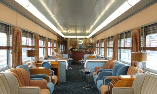 Interior of a vintage train car featuring stylish seating, large windows, and a cozy atmosphere.