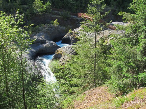 A serene landscape featuring a flowing waterfall surrounded by lush greenery and rocky terrain.