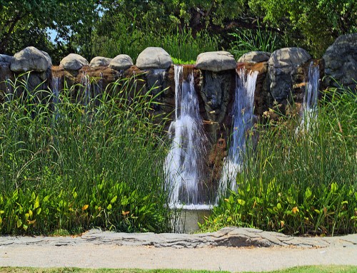 A serene waterfall cascading over rocks, surrounded by lush greenery and tall grasses.