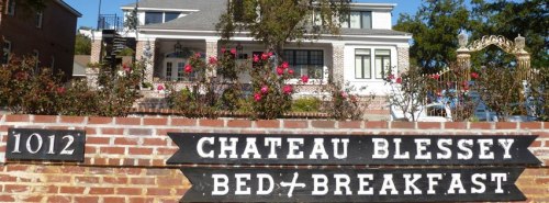 Sign for Chateau Blessey Bed & Breakfast in front of a large, elegant house with blooming flowers.