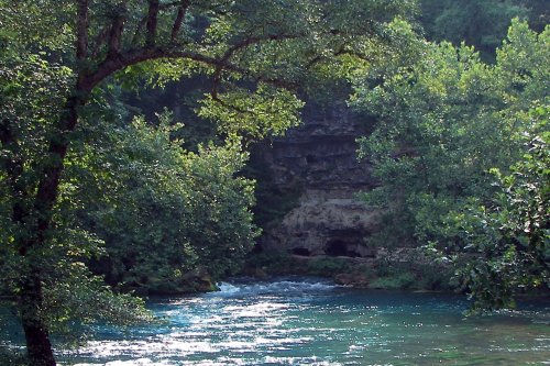 A serene river flows through lush greenery, with rocky cliffs visible in the background.