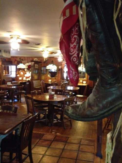 Cozy restaurant interior with wooden tables, cowboy boots hanging, and rustic decor. Warm, inviting atmosphere.